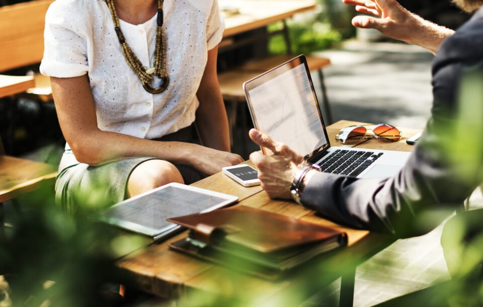 Professionals consulting over a laptop and tablet at an outdoor table.